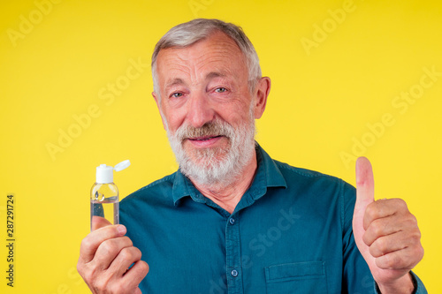 old happy senior man wearing green cotton shirt with a collar and applying alcohol gel to make cleaning and clear germ, bacteria yellow background