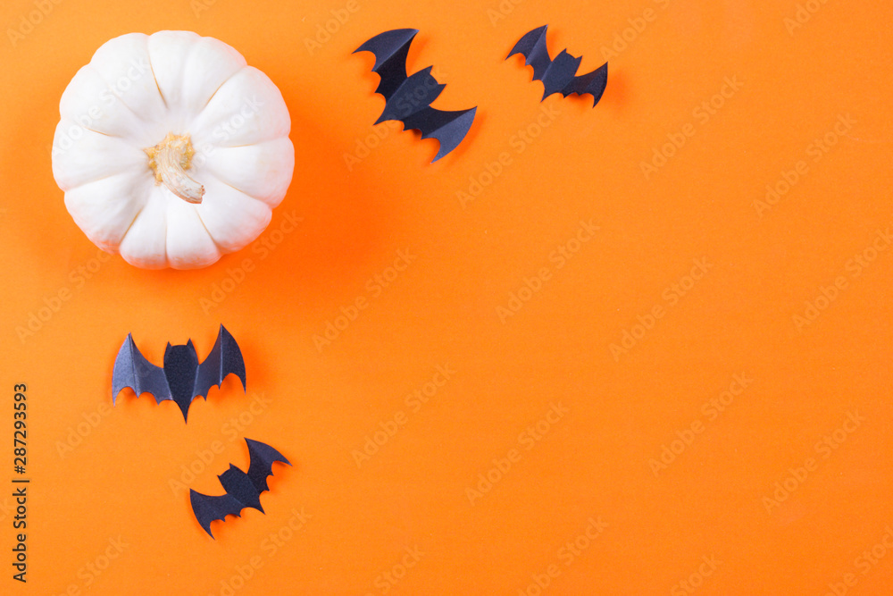Halloween concept. Flock of black paper bats and fresh pumpkin on orange paper background.