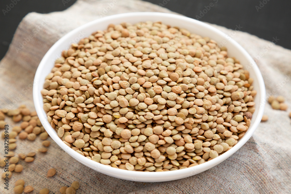 Organic green lentils in a white bowl on a black background, side view. Close-up. Organic green lentils in a white bowl on a black background, side view. Close-up.