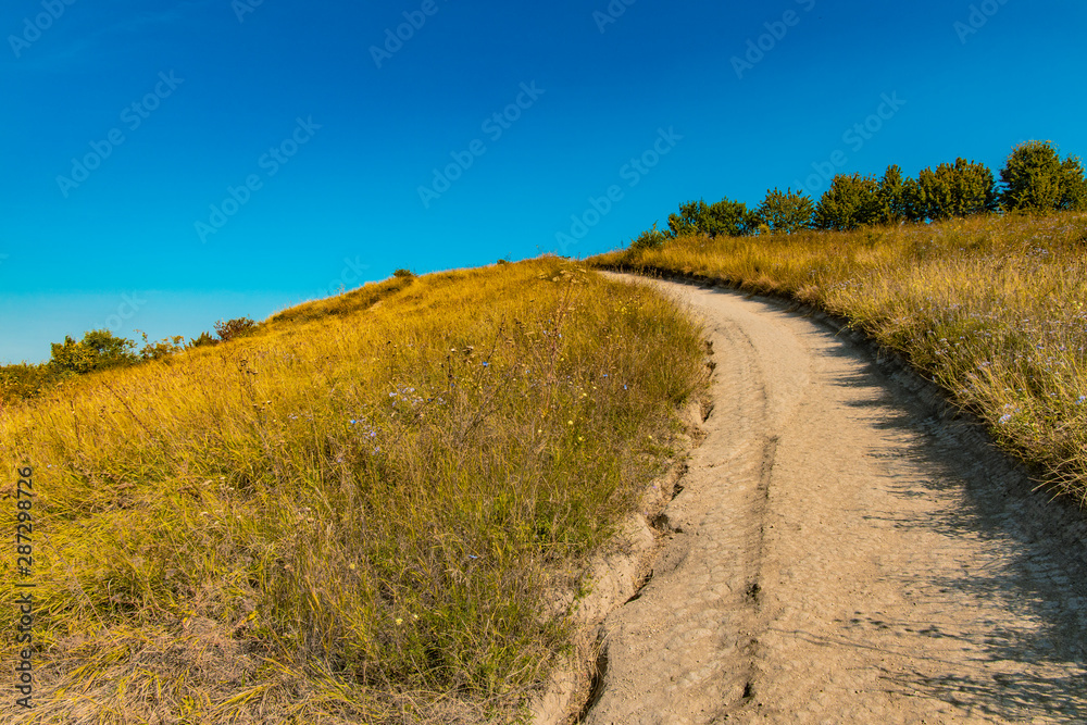 yellow field blue sky rural country side scenic landscape Ukrainian nature environment with curved lonely ground trail through hills 