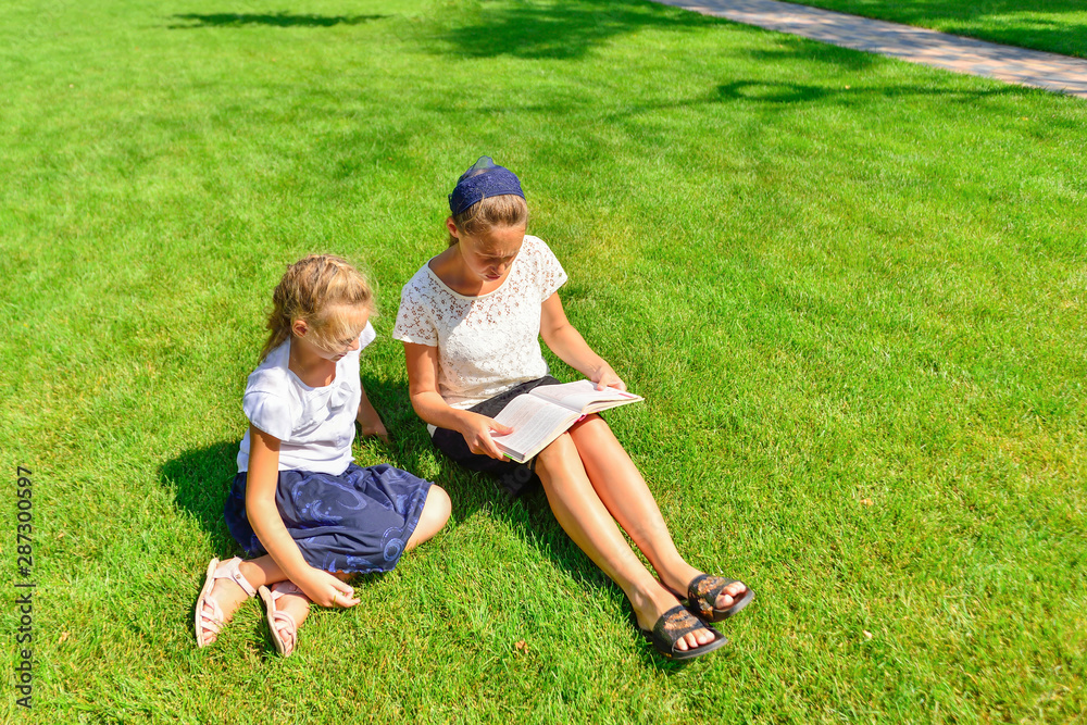 A girl teaches assignments on textbooks and sits on the green grass in the park.