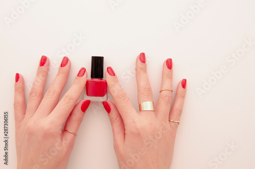 Flat lay groomed woman's hands with red nail varnish bottle isolated on white. Nail varnishing in red color. Manicure concept