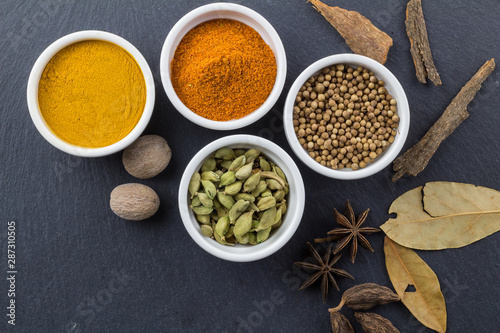 Spices in little white bowls on black slate background - Indian spice top view photo with space for text
