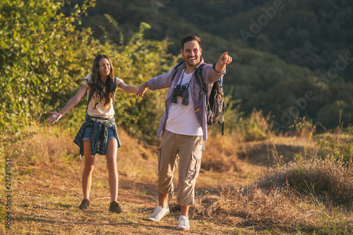 Happy couple is hiking in mountain. Woman is tired and wants a pause.