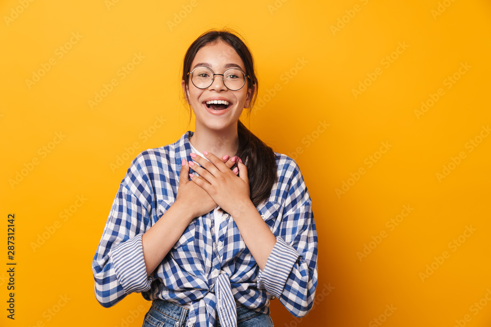 Happy pleased emotional cute teenage girl in glasses posing isolated over yellow wall background. Happy pleased emotional cute teenage girl in glasses posing isolated over yellow wall background.