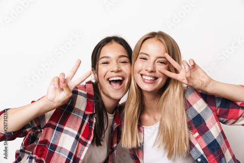 Pretty cheerful happy optimistic young girls friends sisters posing isolated over white wall background showing peace gesture.