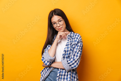 Positive young cute teenage girl in glasses posing isolated over yellow wall background. © Drobot Dean