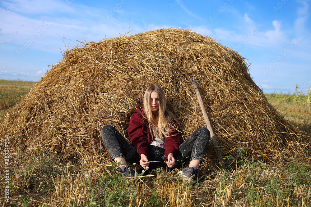 Attractive girl in the guise of a farmer, lounging while sitting on a hay in a field against a blue sky. Attractive girl in the guise of a farmer, lounging while sitting on a hay in a field against a blue sky.