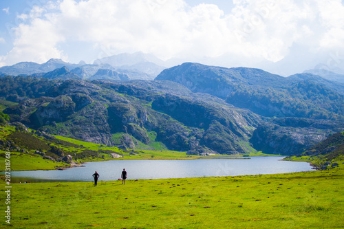 Beautiful view of Ercina Lake in Covadonga Lakes, Asturias, Spain. Green grassland with a couple walking and mountains at the background © Jesus Barroso
