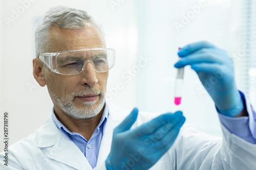 Concentrated bearded scientist staring at pink liquid