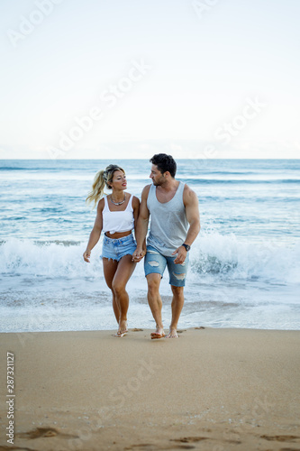 Casual young fit couple walking and talking at the beach during summer vacation.