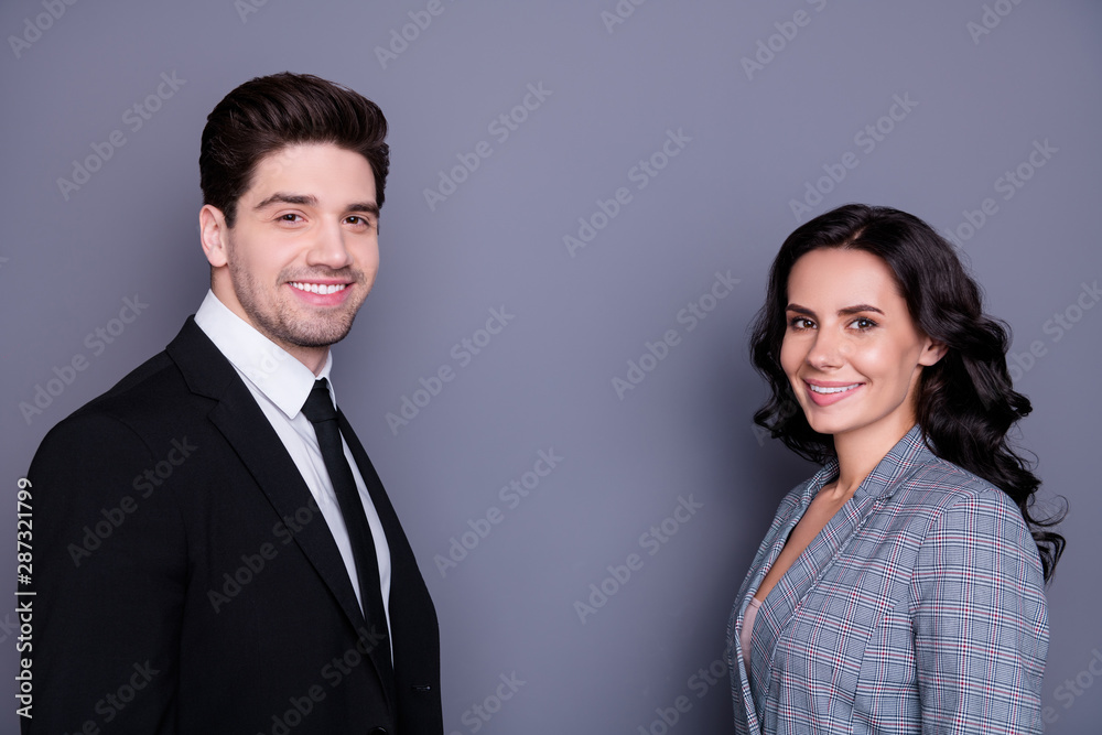 Portrait of beautiful wavy curly brunette haired couple businesspeople looking with toothy smile standing face-to-face wearing black blazer tie jacket isolated over grey background Portrait of beautiful wavy curly brunette haired couple businesspeople looking with toothy smile standing face-to-face wearing black blazer tie jacket isolated over grey background