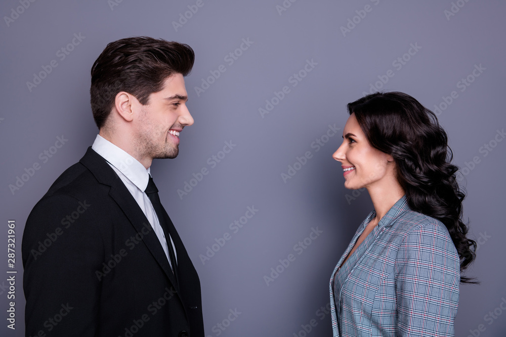 Profile side photo of charming business people with brunette hair wavy curly hairstyle looking standing face-to-face wearing black tux jacket blazers isolated over grey background