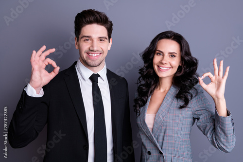 Portrait of beautiful two bussinesspeople showing ok sign wearing stylish black jacket blazer tie isolated over gray background photo
