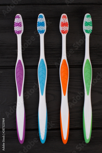 Four colorful toothbrushes on black background. Group of different brushes for cleaning teeth. Dental health concept.