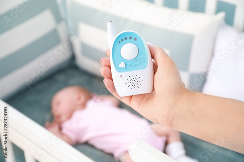 Mother holding radio nanny near bed with sleeping baby
