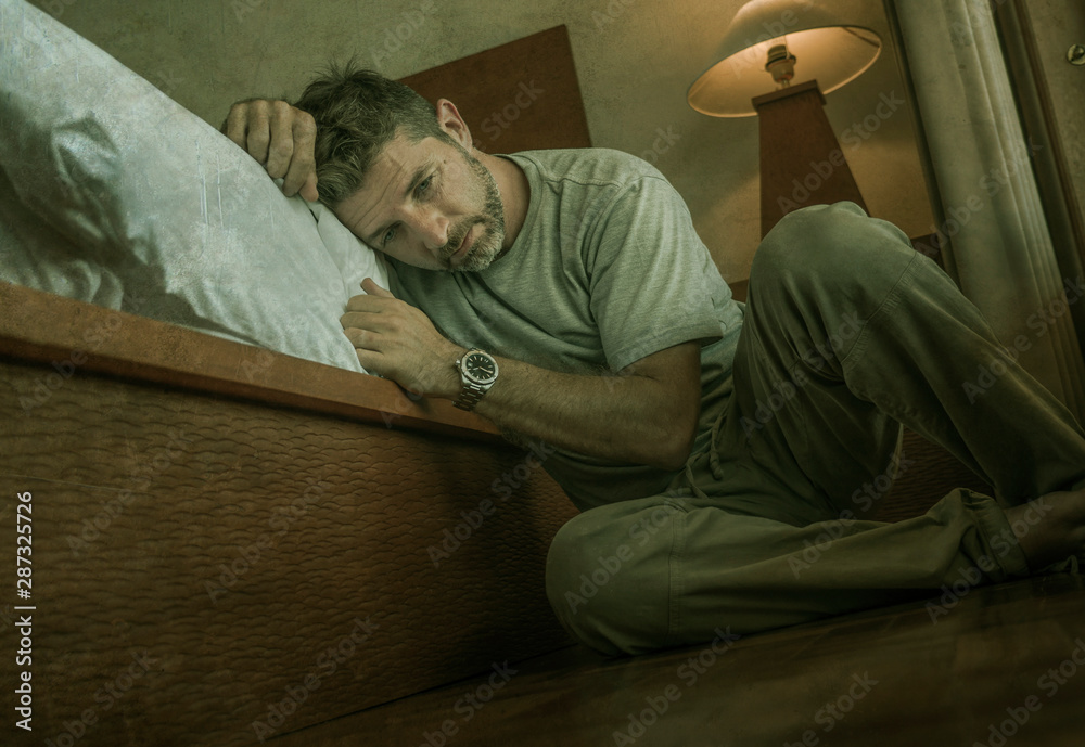 young depressed and desperate man sitting on bedroom floor next to bed suffering depression and anxiety feeling overwhelmed and helpless young depressed and desperate man sitting on bedroom floor next to bed suffering depression and anxiety feeling overwhelmed and helpless