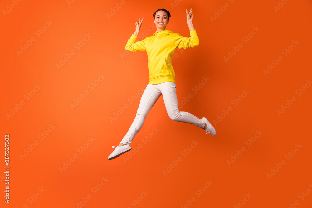 Full body photo of cheerful lady making v-signs smiling jumping isolated over orange background