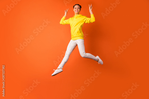 Full body photo of cheerful lady making v-signs smiling jumping isolated over orange background © deagreez