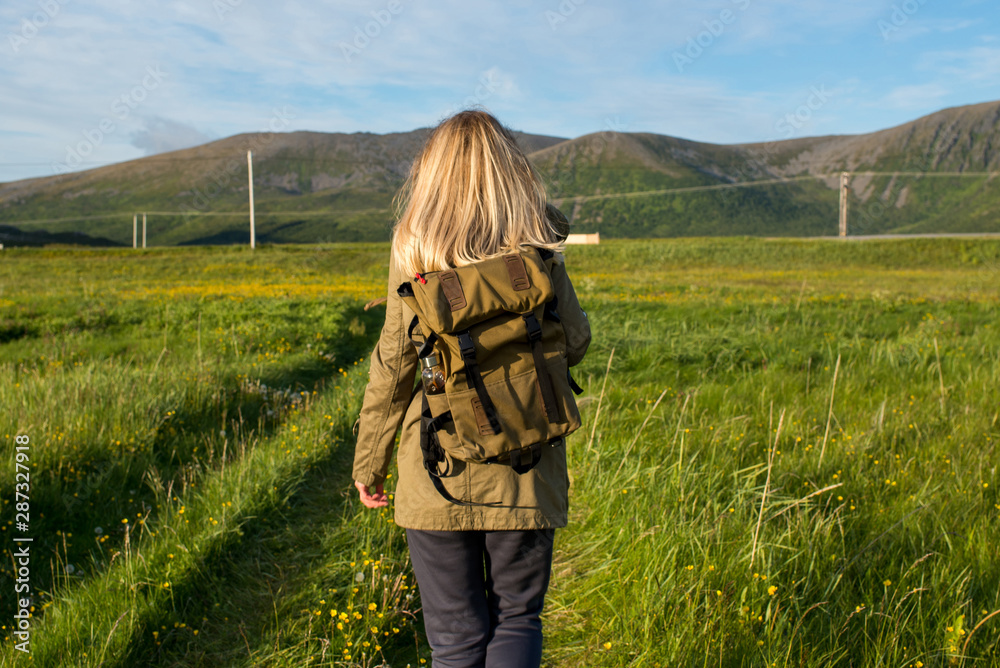 Blond hair women with backpack enjoys scenic view. Beautiful nature landscape. Green grass, mountain. Lonely women. Enjoy moment, relaxation. Travel and adventure. Explore Norway. Lofoten Islands
