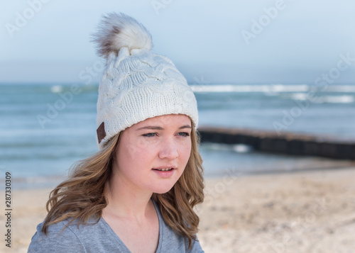 Female model wearing white knitted beanie with Bluetooth speakers inside, listening to music outdoors. © MWolf Images