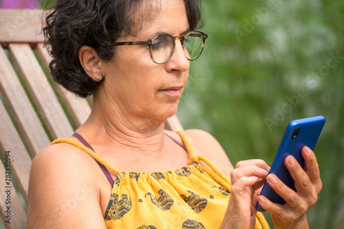 mature woman relaxing in a garden holding and using smartphone mobile
