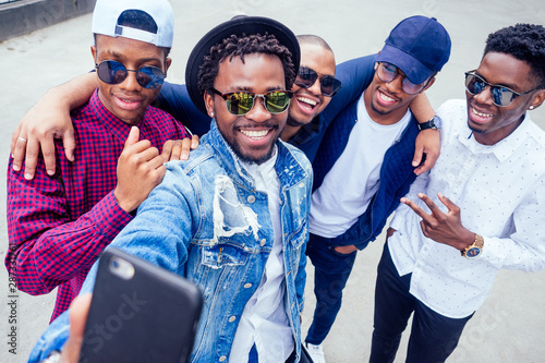 a group of five fashionable cool African American guys students communicating on the street looking at smartphone take pictures selfie on phone in street