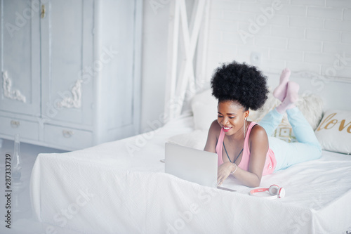 Young african american woman lying on the bed while working on laptop.