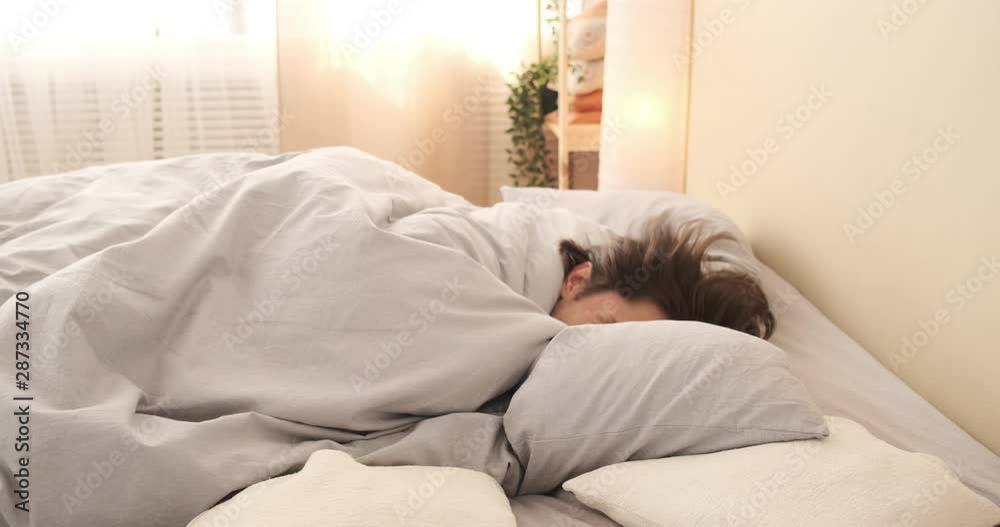 Exhausted young man falling asleep with quilt on bed
