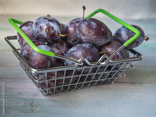 Fresh plums with a metal basket on a gray table closeup