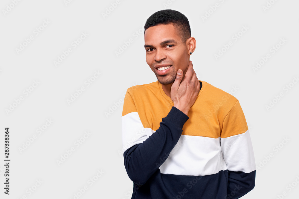 Smiling African American man touching his neck with hand after shaving and looking to the camera while standing against white studio background. Good-looking Afro male feeling clean and fresh. Smiling African American man touching his neck with hand after shaving and looking to the camera while standing against white studio background. Good-looking Afro male feeling clean and fresh.