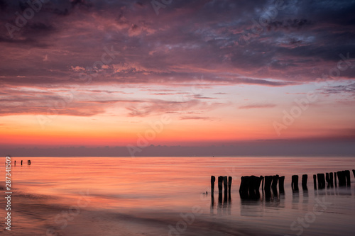 Colorful sunrise at beach of baltic sea in summer with silhouette of old poles groins, Groemitz, Schleswig-Holstein, Germany