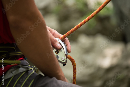 Mountain rock climbing detail. Focus on the hand of the belayer holding the rope with a security device.