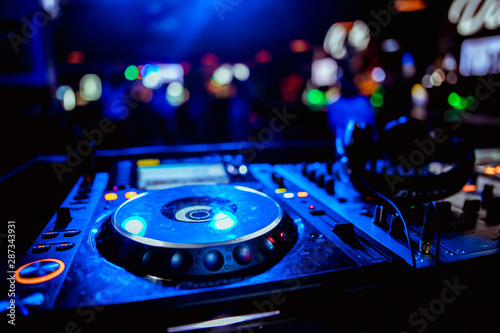 Close up view of the hands of a male disc jockey mixing music on his deck with his hands poised over the vinyl record on the turntable and the control switches at night