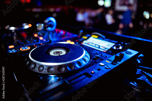 Close up view of the hands of a male disc jockey mixing music on his deck with his hands poised over the vinyl record on the turntable and the control switches at night