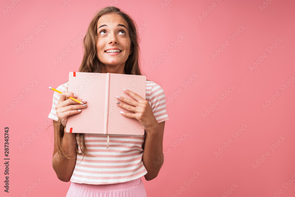 Image of amazed pretty woman wearing striped t-shirt looking upward while holding diary and pencil Image of amazed pretty woman wearing striped t-shirt looking upward while holding diary and pencil