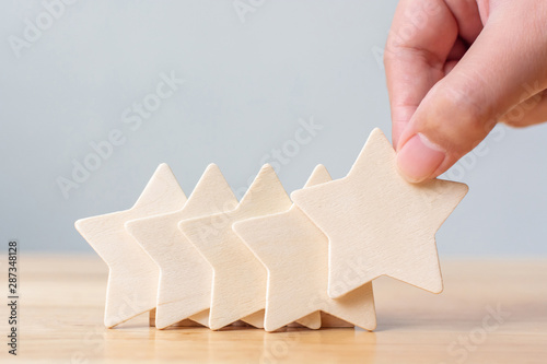Hand putting wooden five star shape on table. The best excellent business services rating customer experience concept photo