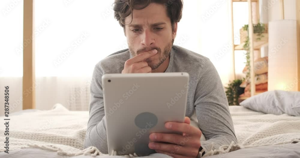Man using digital tablet lying on bed in the morning Man using digital tablet lying on bed in the morning