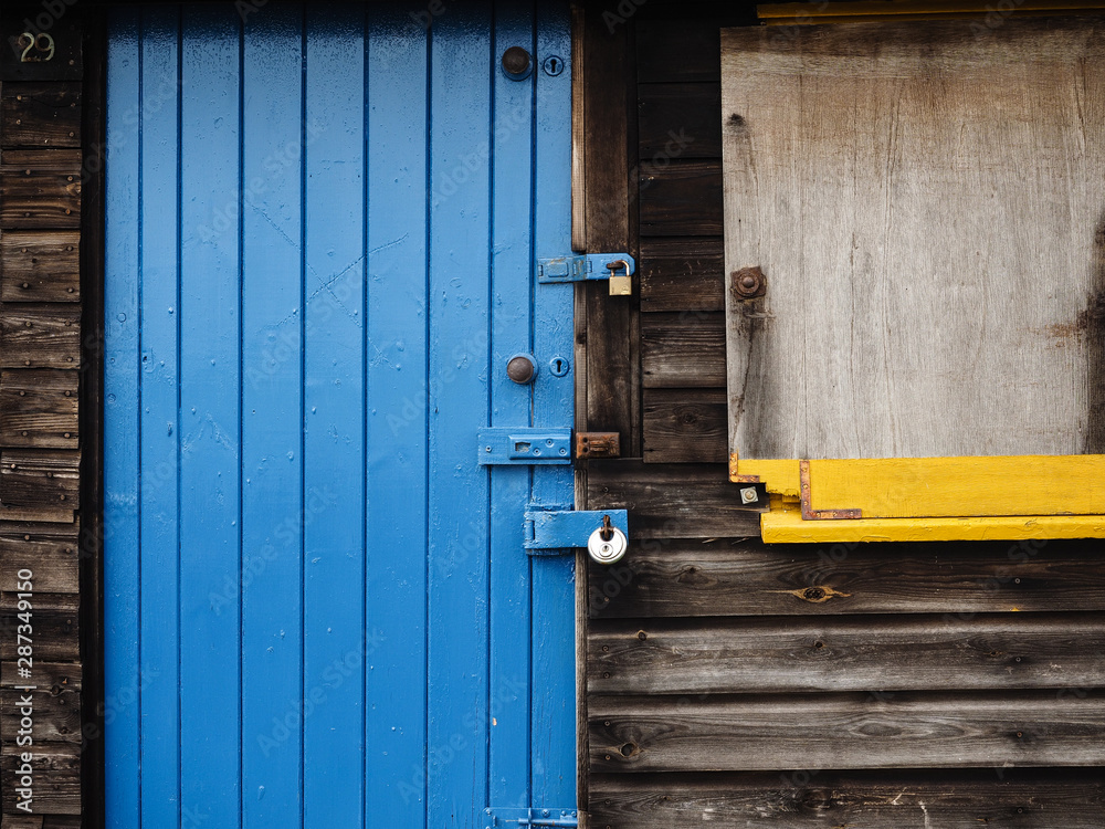 Blue door on a bleached black wooden shed with a yellow window sill Blue door on a bleached black wooden shed with a yellow window sill