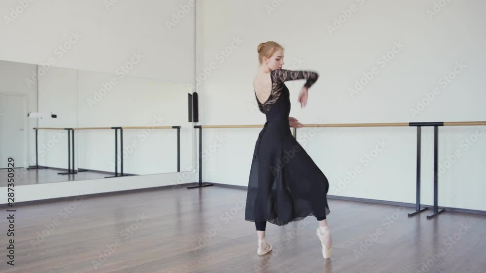 Beautiful ballerina in black lace leotard, long wrap skirt and pointe shoes dancing gracefully during rehearsal in ballet dance studio Beautiful ballerina in black lace leotard, long wrap skirt and pointe shoes dancing gracefully during rehearsal in ballet dance studio