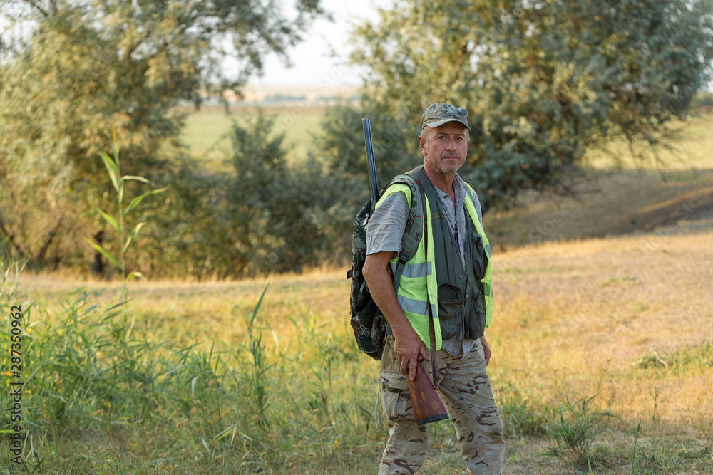 Hunting period, autumn season open. A hunter with a gun in his hands in hunting clothes in the autumn forest in search of a trophy. A man stands with weapons and hunting dogs tracking down the game.	