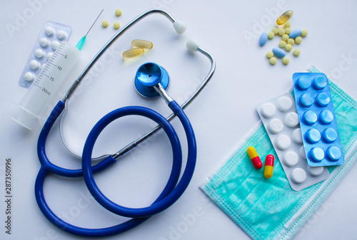 Top view of flat lay: medical supplies doctor, funds for the treatment of the patient - the stethoscope, protective mask, pills, thermometer, syringe on the background of a white textured rough sheet