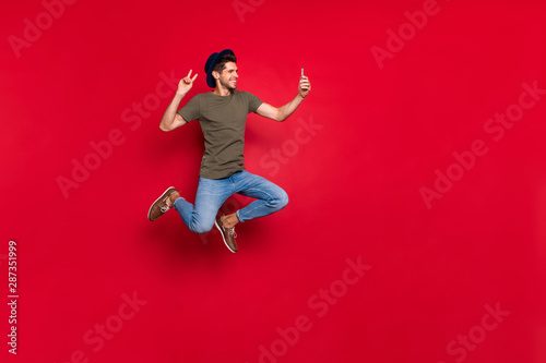 Full size photo of cool guy jumping high making selfies show v-sign wear casual outfit isolated on red background