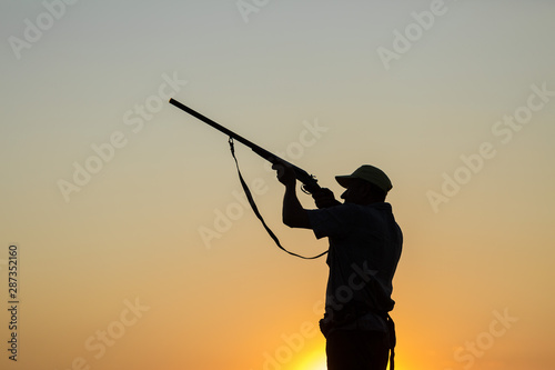  Hunting period, autumn season open. A hunter with a gun in his hands in hunting clothes in the autumn forest in search of a trophy. A man stands with weapons and hunting dogs tracking down the game.