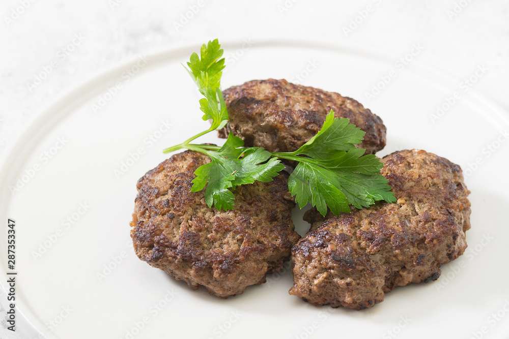Beef patties on a white plate. Grey table. Top view