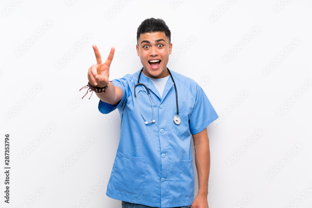 Young surgeon doctor man over isolated white wall smiling and showing victory sign Young surgeon doctor man over isolated white wall smiling and showing victory sign