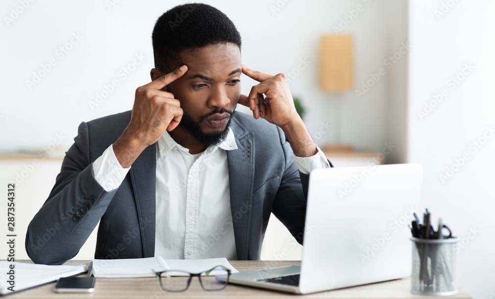 Concentrated african employee analyzing information on laptop, working in office Concentrated african employee analyzing information on laptop, working in office