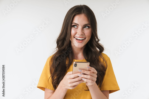 Optimistic dreaming young emotional woman posing isolated over white wall background using mobile phone.
