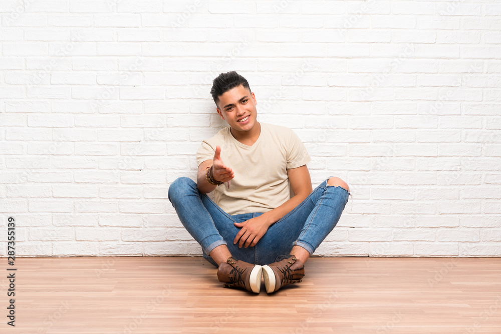 Young man sitting on the floor handshaking after good deal Young man sitting on the floor handshaking after good deal