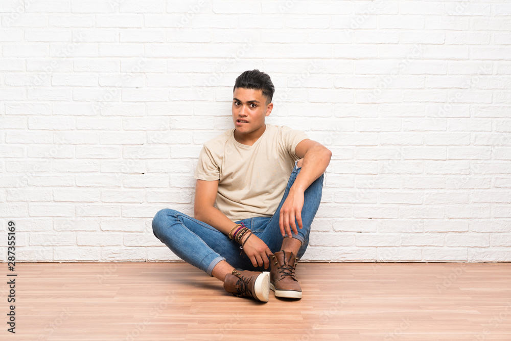 Young man sitting on the floor having doubts and with confuse face expression Young man sitting on the floor having doubts and with confuse face expression